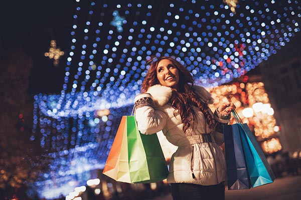 Cheerful young woman with colorful shopping bags having fun in the city street at Christmas time.